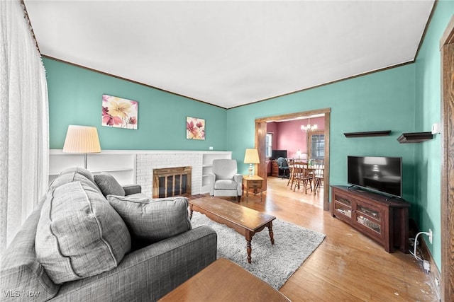 living room featuring a brick fireplace, wood finished floors, and a chandelier