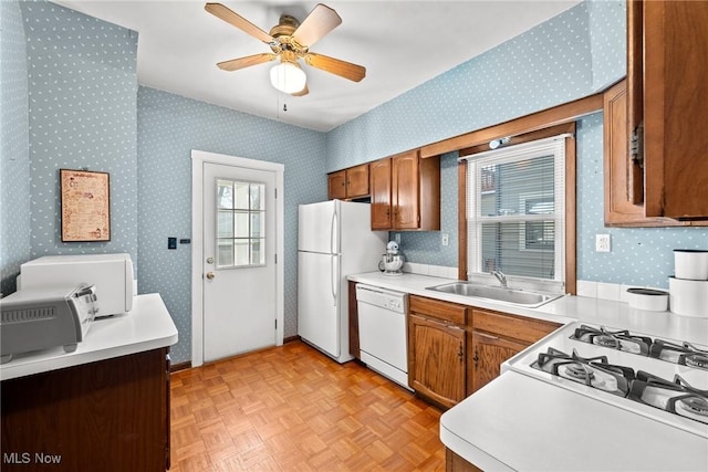 kitchen featuring brown cabinetry, white appliances, ceiling fan, wallpapered walls, and a sink