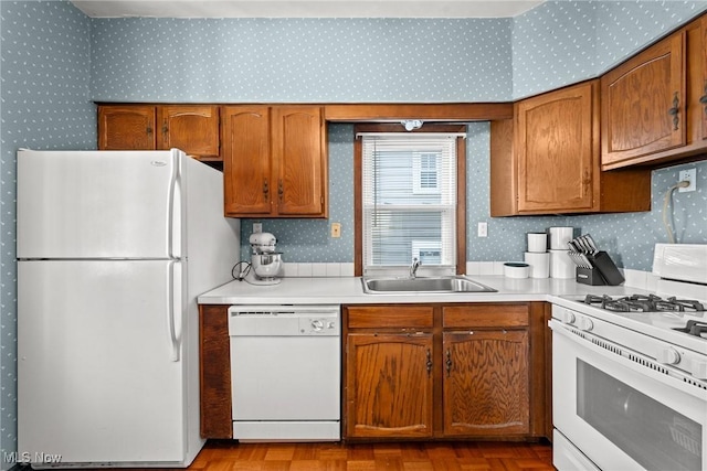 kitchen with brown cabinetry, a sink, light countertops, wallpapered walls, and white appliances