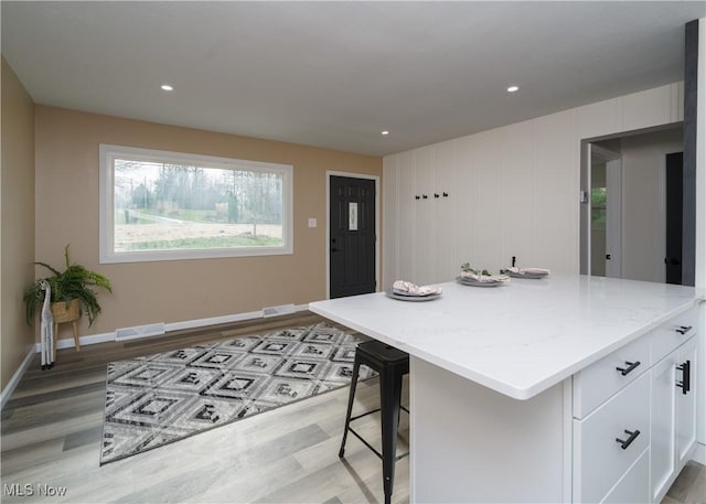 kitchen with light stone countertops, white cabinetry, baseboards, light wood-type flooring, and visible vents