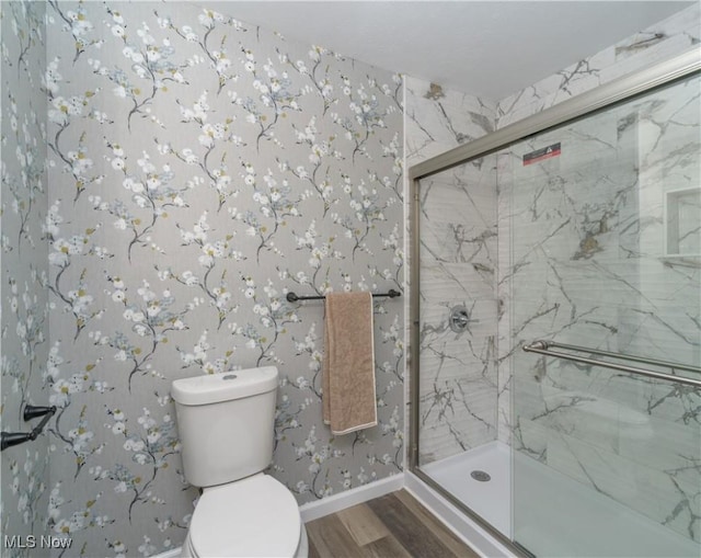 bathroom featuring wood finished floors, baseboards, toilet, a marble finish shower, and wallpapered walls