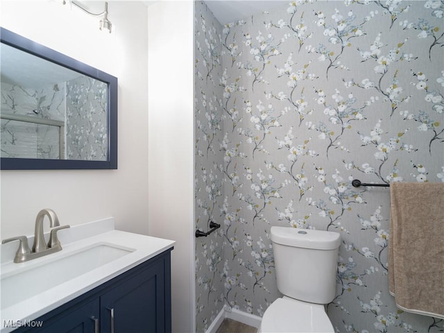 full bathroom with toilet, a stall shower, baseboards, and vanity