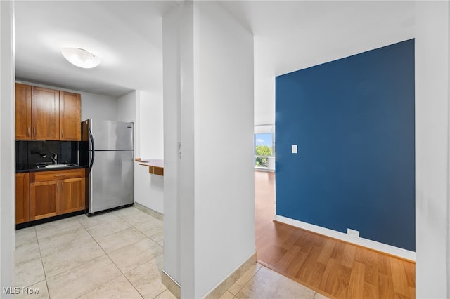 kitchen with brown cabinets, light tile patterned flooring, a sink, freestanding refrigerator, and decorative backsplash