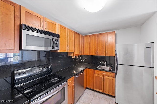 kitchen with dark countertops, a sink, stainless steel appliances, light tile patterned floors, and backsplash
