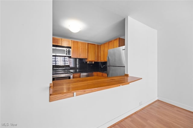 kitchen featuring decorative backsplash, wood finished floors, baseboards, a peninsula, and stainless steel appliances