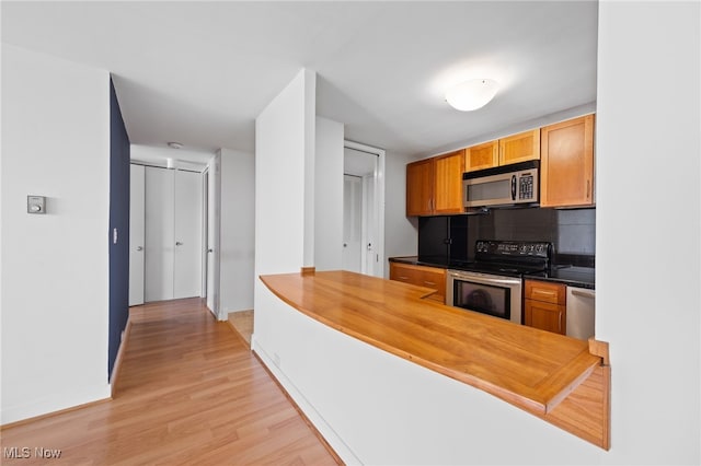 kitchen with a peninsula, baseboards, light wood-style flooring, backsplash, and stainless steel appliances