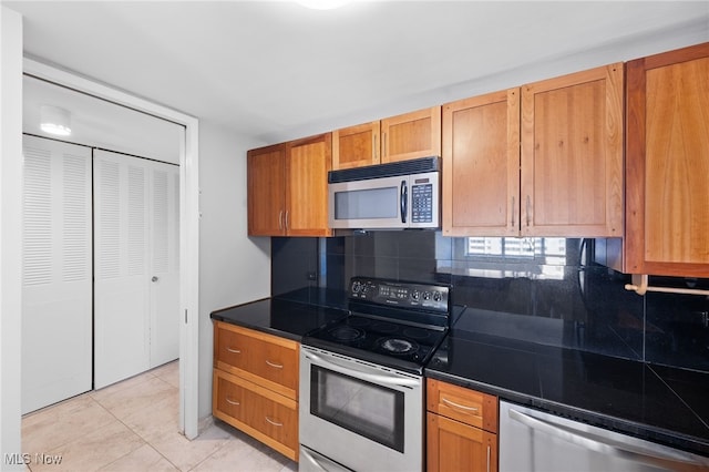 kitchen with appliances with stainless steel finishes, brown cabinets, dark countertops, and tasteful backsplash