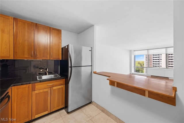 kitchen with freestanding refrigerator, a sink, brown cabinets, and dark countertops