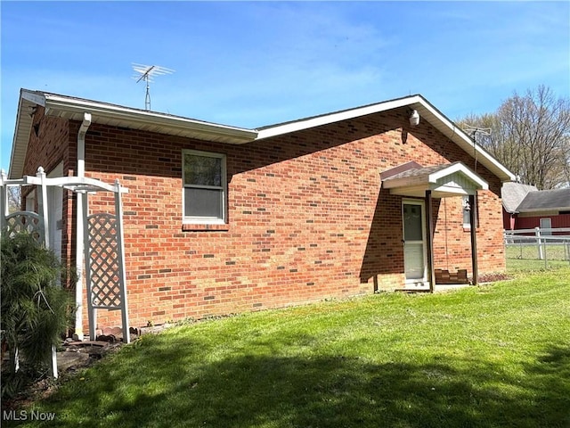 rear view of house with a lawn, fence, and brick siding