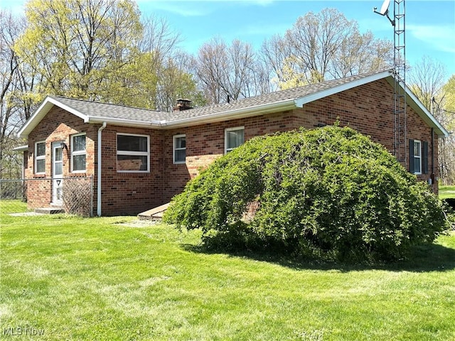 view of side of home with a chimney, a yard, and brick siding