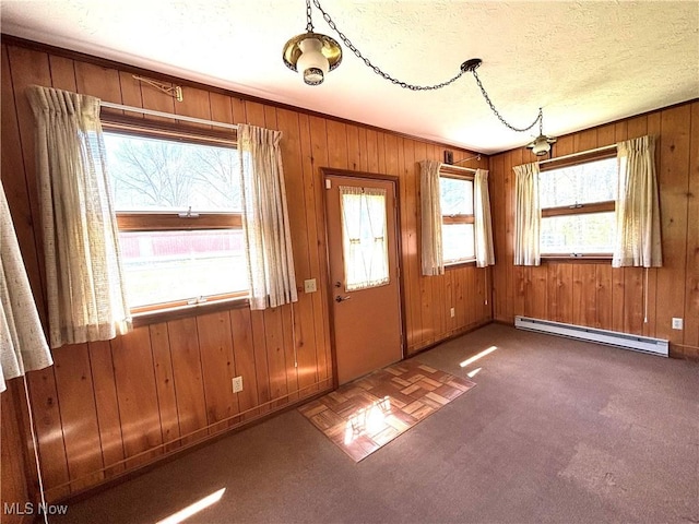 empty room with wooden walls, a textured ceiling, carpet, baseboards, and a baseboard heating unit