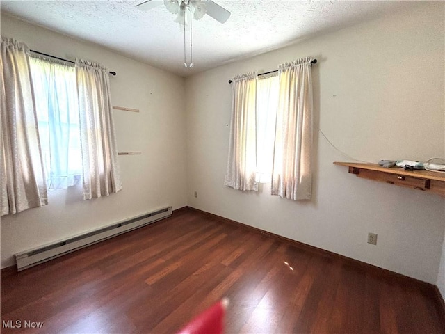 unfurnished room with plenty of natural light, baseboard heating, dark wood-style floors, and a textured ceiling