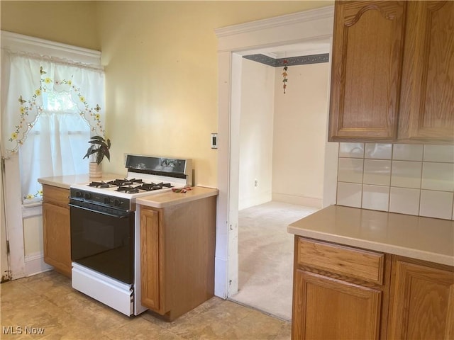 kitchen with brown cabinets, light carpet, light countertops, white gas stove, and baseboards