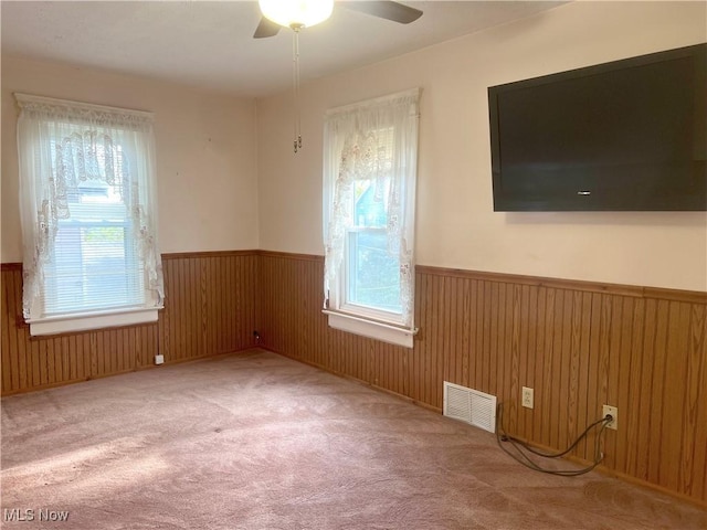 spare room featuring a ceiling fan, visible vents, a wainscoted wall, carpet floors, and wooden walls