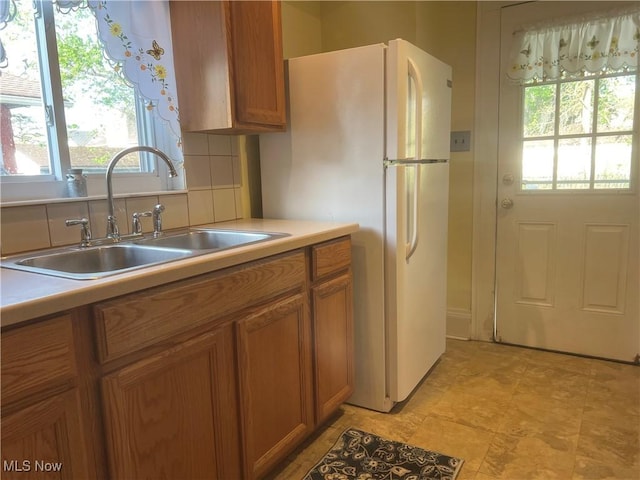 kitchen with brown cabinetry, a sink, freestanding refrigerator, and light countertops