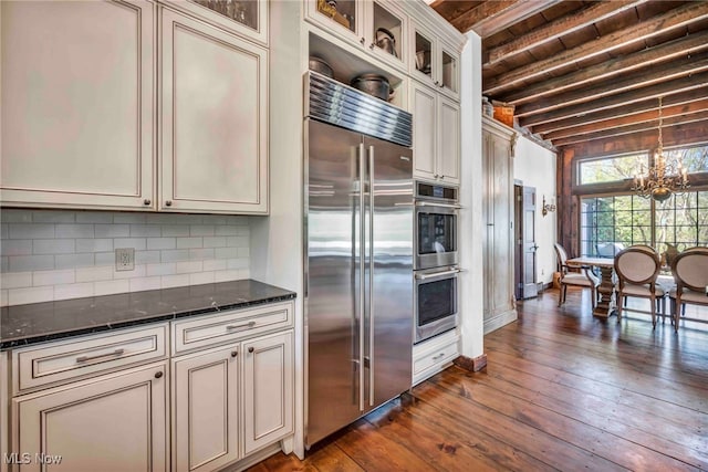 kitchen with decorative backsplash, beamed ceiling, dark wood finished floors, dark stone countertops, and stainless steel appliances
