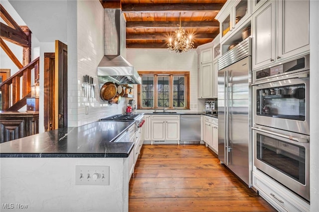 kitchen with a peninsula, hardwood / wood-style floors, a sink, appliances with stainless steel finishes, and a notable chandelier