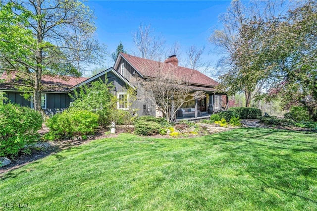rear view of property with outdoor lounge area, board and batten siding, a yard, and a chimney