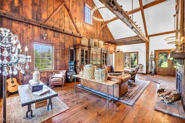 living area with hardwood / wood-style flooring, high vaulted ceiling, beamed ceiling, a notable chandelier, and wooden walls