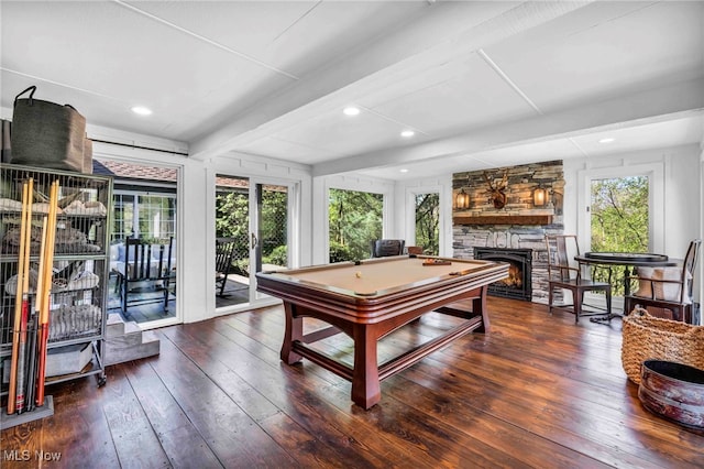 game room featuring beamed ceiling, a stone fireplace, hardwood / wood-style floors, and a wealth of natural light