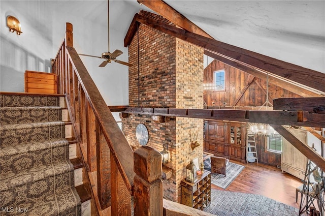unfurnished living room featuring ceiling fan, high vaulted ceiling, wood finished floors, beamed ceiling, and stairway