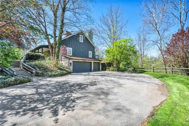 view of side of property with board and batten siding, driveway, a chimney, a garage, and fence