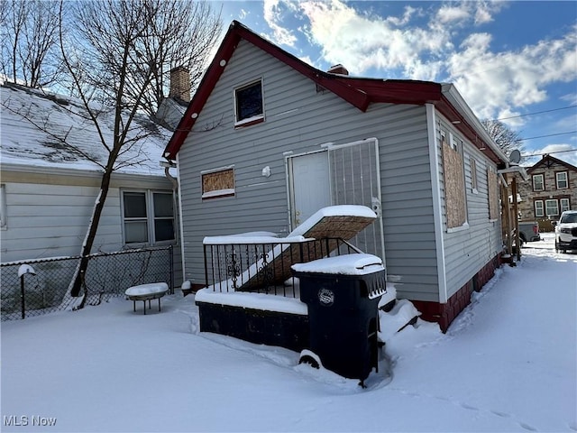 snow covered house featuring fence and a chimney
