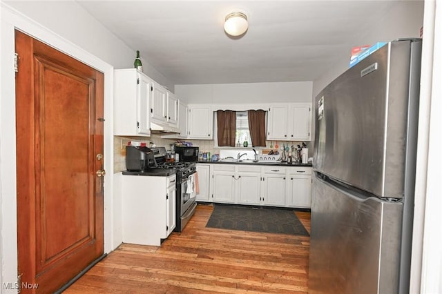 kitchen featuring under cabinet range hood, stainless steel appliances, dark countertops, and dark wood-type flooring