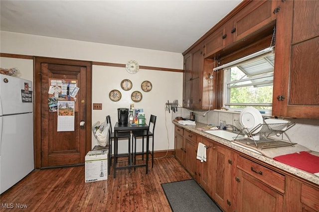 kitchen with a sink, light countertops, freestanding refrigerator, and dark wood-style flooring