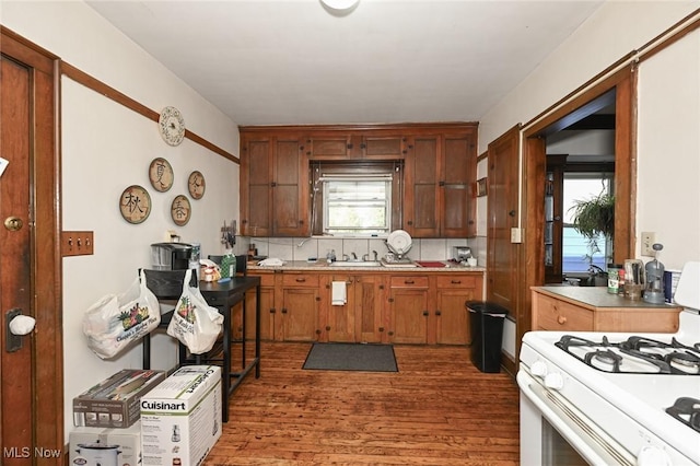 kitchen with light wood-type flooring, light countertops, white gas stove, and tasteful backsplash