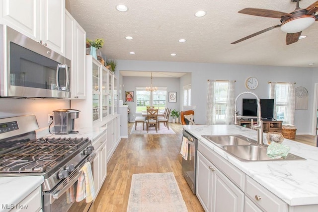 kitchen with a textured ceiling, appliances with stainless steel finishes, a sink, white cabinets, and light wood finished floors