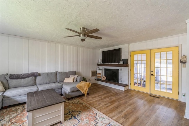 living area with wood walls, a textured ceiling, hardwood / wood-style flooring, french doors, and a ceiling fan