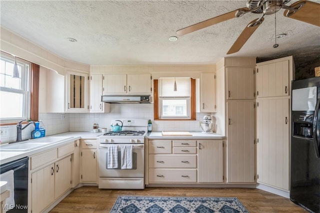 kitchen with light countertops, a textured ceiling, under cabinet range hood, a sink, and black appliances