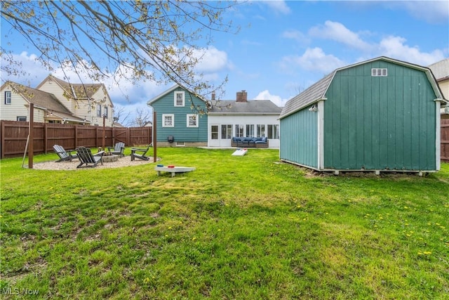 rear view of house featuring a fire pit, fence, a storage unit, an outbuilding, and a yard