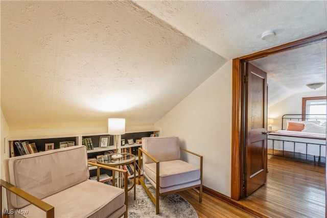 sitting room featuring a textured ceiling, baseboards, lofted ceiling, and hardwood / wood-style floors