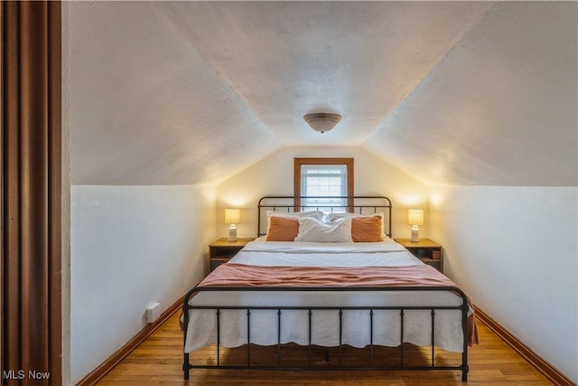 bedroom with baseboards, wood finished floors, and lofted ceiling