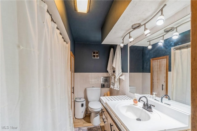 full bath featuring vanity, a wainscoted wall, toilet, and tile walls