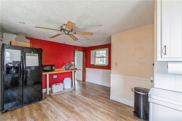 kitchen featuring white cabinets, ceiling fan, light wood-style floors, a wainscoted wall, and black appliances