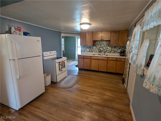 kitchen featuring a sink, white appliances, light countertops, brown cabinetry, and dark wood-type flooring