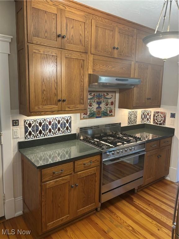 kitchen with under cabinet range hood, brown cabinetry, and stainless steel gas range oven