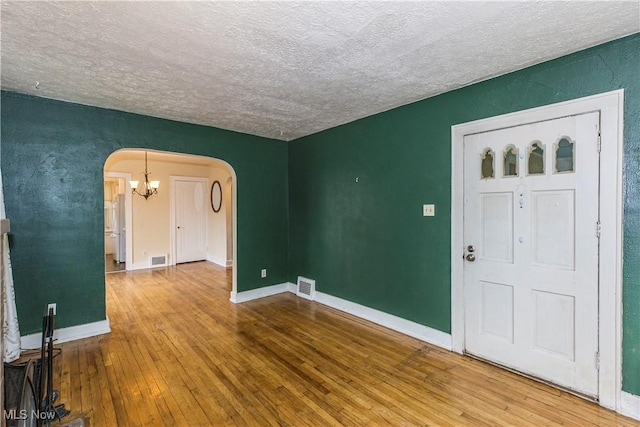 interior space featuring arched walkways, a textured ceiling, hardwood / wood-style floors, and visible vents