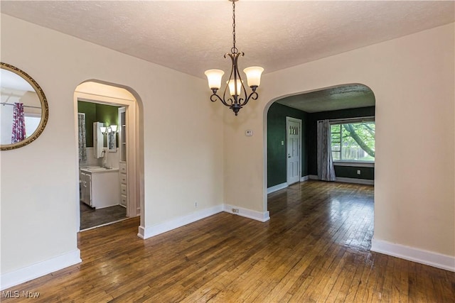 empty room with arched walkways, a textured ceiling, an inviting chandelier, and hardwood / wood-style floors