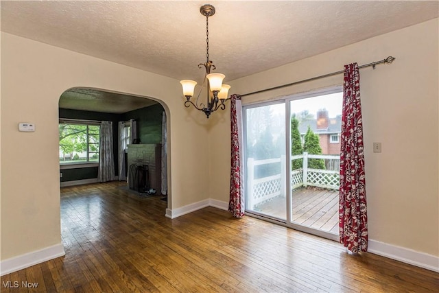 unfurnished dining area featuring arched walkways, baseboards, and hardwood / wood-style flooring