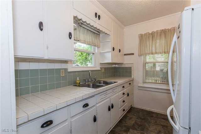 kitchen with backsplash, a sink, white cabinets, freestanding refrigerator, and tile counters