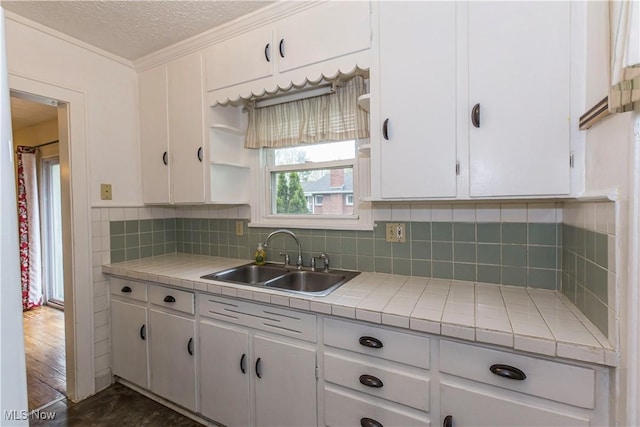 kitchen with tile counters, a sink, and white cabinets
