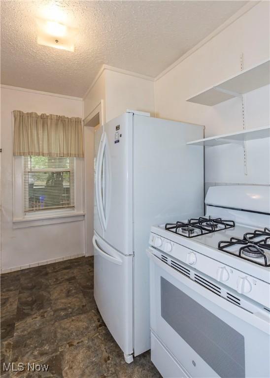 kitchen with a textured ceiling, white range with gas stovetop, and stone finish floor
