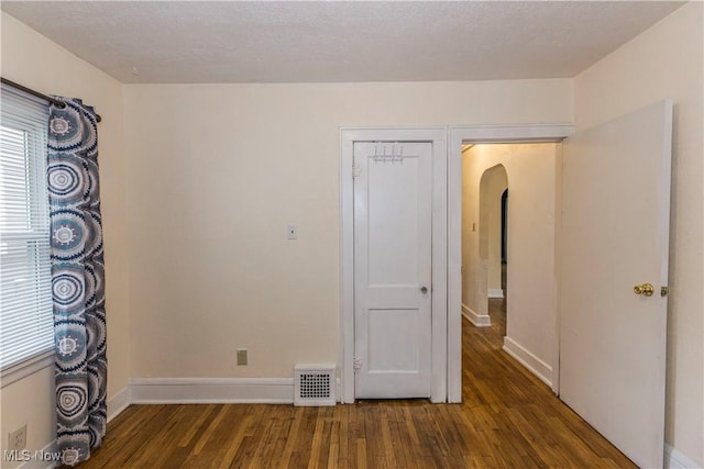 empty room featuring arched walkways, baseboards, visible vents, and wood finished floors