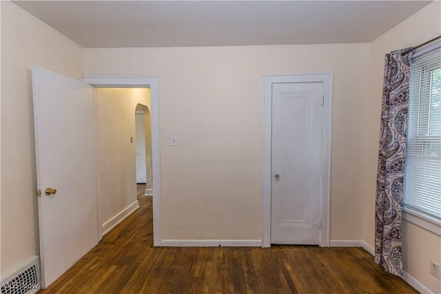 unfurnished bedroom with arched walkways, baseboards, visible vents, and wood finished floors