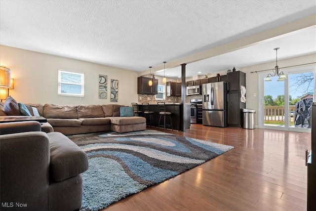 living room featuring a textured ceiling, a notable chandelier, a healthy amount of sunlight, and dark wood-type flooring