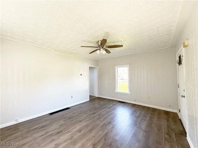empty room with dark wood-style flooring, a textured ceiling, a ceiling fan, baseboards, and visible vents